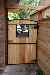 Wooden arch top door-style gate with custom Zia metal window insert with tongue and groove wooden privacy fence with double open top rail.